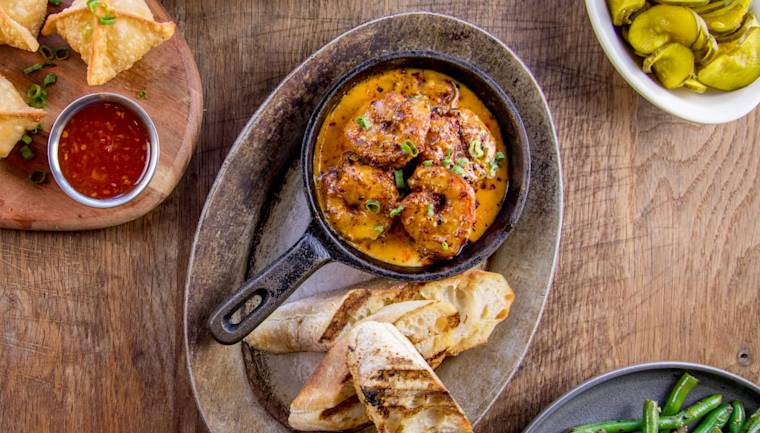 Table set with food, including shrimp and grits with bread, green beans, wontons with chili sauce, and pickles