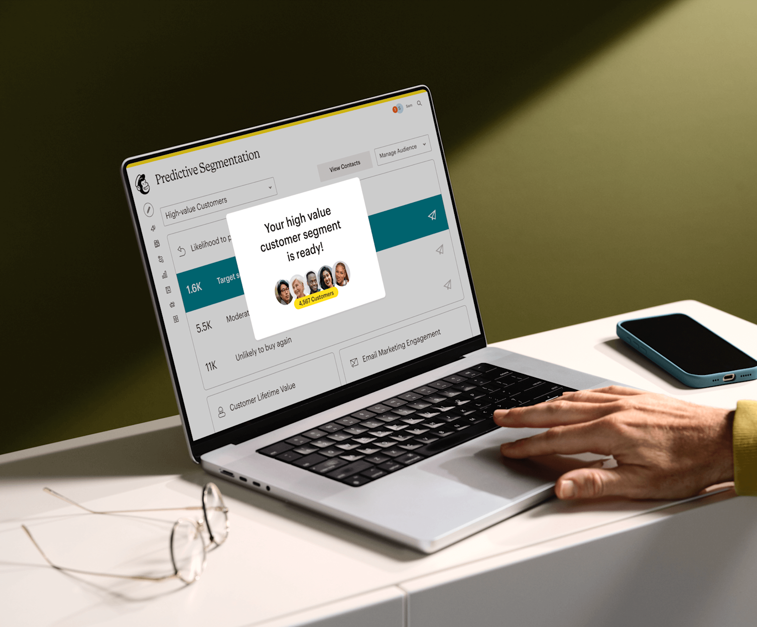 Image of a person sitting at a desk, looking at a laptop screen displaying Mailchimp’s Predictive Segmentation feature. The visual shows a display indicating that the user’s high value customer segment is ready to view. 